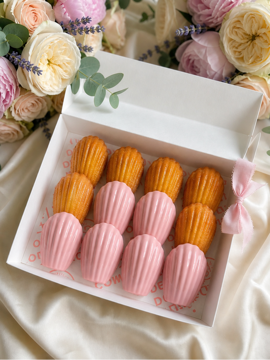 Box of pink and orange pastries with a bouquet of flowers in the background